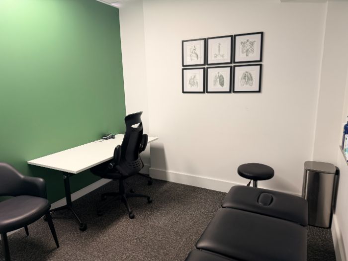 A consulting room with desk, chairs and blood pressure monitor