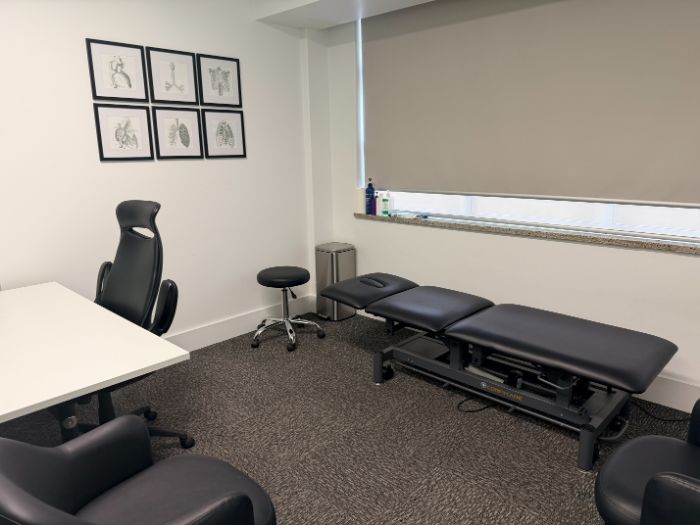 A consulting room with treatment table, stool and framed anatomical prints